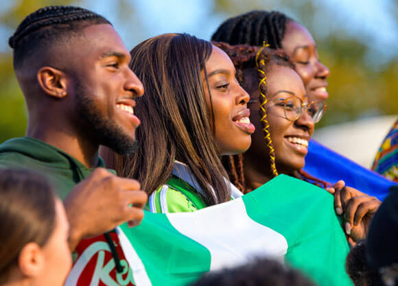 A group of international students hold flags from their country and smile together